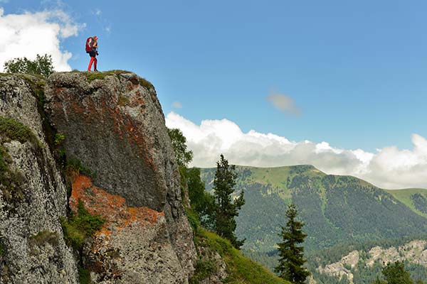 person hiking standing on top of a hill cliff looking into the green valleys of borjomi-kharagauli national park georgia