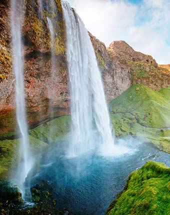 cascading waterfall into blue pool below with green grass and high rocks on a trip to iceland