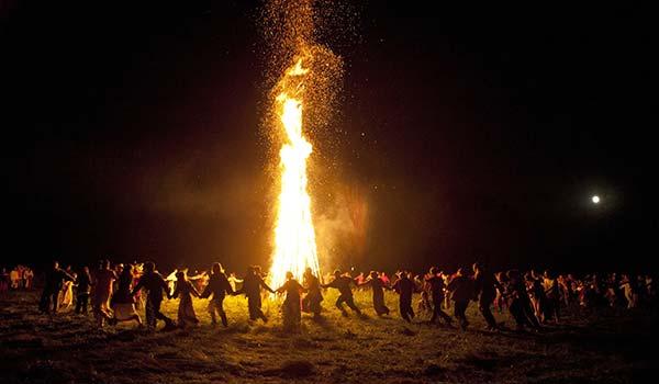 people holding hands dancing in a circle around a bonfire for summer solstice in iceland