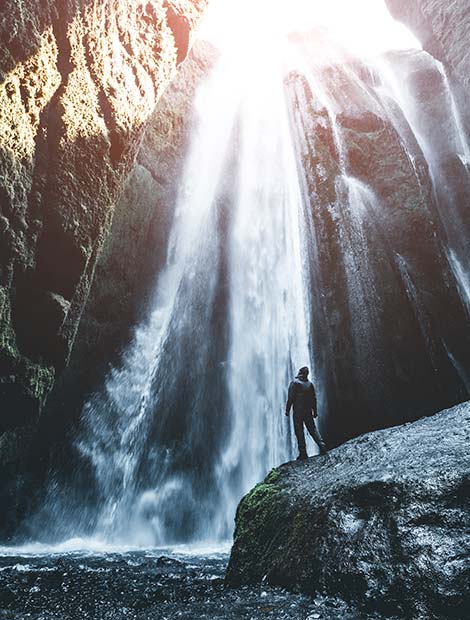 solo traveller on a group tour in iceland looking up at a powerful waterfall