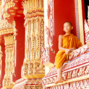 a young monk sits on a temple window looking onto the landscape of cambodia