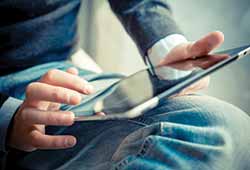 What to pack on a group holiday to Europe. A man wearing blue jeans and a blue jumper holding an ipad or a kindle